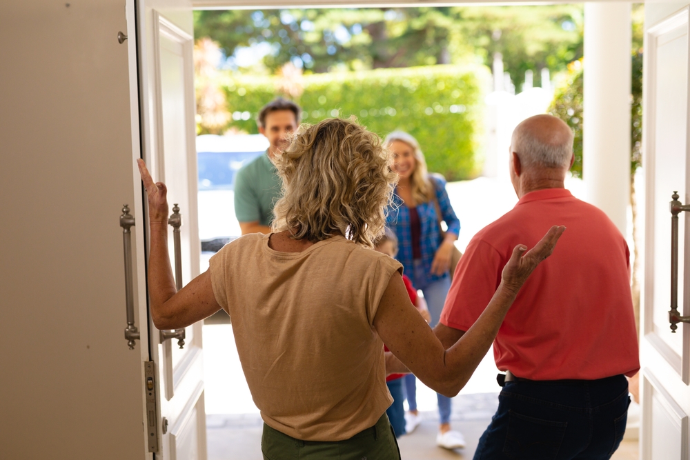 Rear View Of Senior Couple Welcoming Their Family At Home.